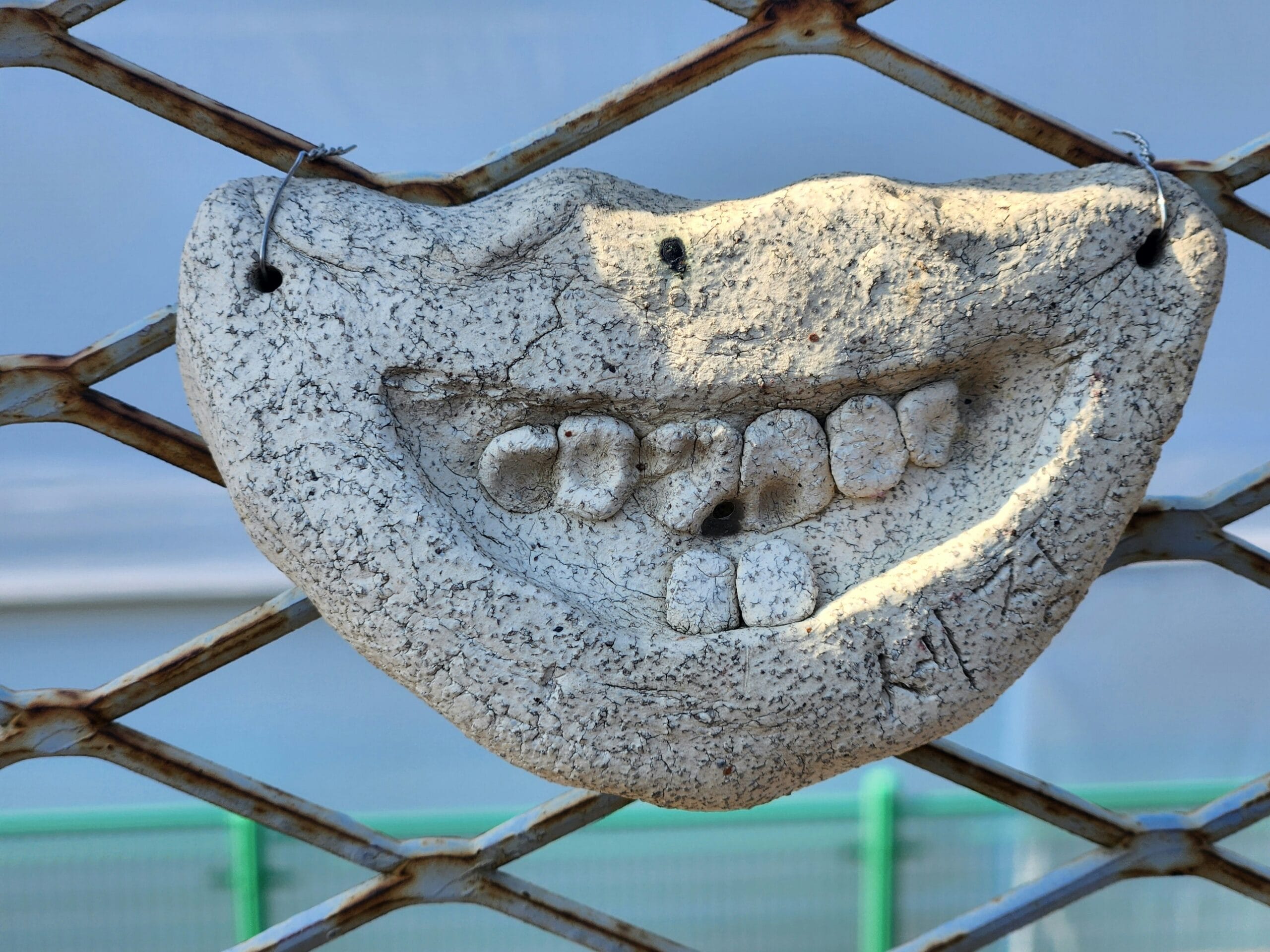 A smiling stone face hangs on a metal grate.